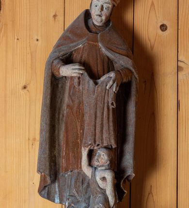 Zdjęcie nr 1: Rzeźba pełnoplastyczna, ścięta z tyłu, ustawiona na niewielkiej podstawie o nieregularnym kształcie. Biskup ukazany w całej postaci, frontalnie w postawie stojącej. U jego stóp po prawej stronie kompozycji przedstawiona w pomniejszonej skali postać klęczącego żebraka. Głowa św. Marcina lekko pochylona do dołu. Święty w ugiętych łokciach rękach trzyma przed sobą szatę, którą zamierza nałożyć klęczącemu żebrakowi. Twarz biskupa podłużna o wyraźnie zaznaczonym, lekko zaokrąglonym podbródku, krótkim nosie oraz lekko rozchylonych ustach; pozbawiona zarostu. Biskup ubrany jest w długą albę, złoconą dalmatykę sięgającą za kolana oraz złoty, podbity srebrną tkaniną płaszcz sięgający ziemi. Na głowie świętego przedstawiona infuła biskupia. Na dłoniach rękawiczki. Spod alby widoczna prawa stopa w obuwiu o zaokrąglonych noskach. Żebrak przedstawiony jako brodaty mężczyzna o okrągłej, pozbawionej włosów głowie. Swój wzrok kieruje ku górze, w kierunku św. Marcina. Prawą, uniesioną do góry ręką chwyta brzeg szaty nakładanej mu przez świętego. Lewa ręka, wsparta na kuli, opuszczona wzdłuż tułowia. Przez prawe ramię  postaci przewieszona srebrna szata, luźno okrywająca ciało. Tors odsłonięty.

