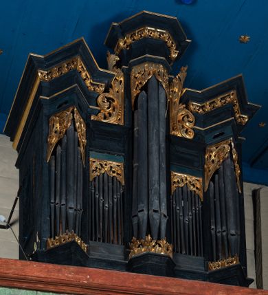 Zdjęcie nr 1: Prospekt organowy o formach architektonicznych, pięcioosiowy, jednokondygnacyjny ze zwieńczeniem. Osie nieparzyste wypukłe; osie skrajne na rzucie trójkąta; oś środkowa wyższa na rzucie połowy sześcioboku ujęta w górnej części akantowymi wolutami. W osiach parzystych niższe płyciny mieszczące mniejsze piszczałki. W górnej partii części piszczałkowej płaskorzeźbiona dekoracja akantowa. Zwieńczenie utworzone z przełamującego się, bogato profilowanego belkowania z wydatnym gzymsem. Struktura malowana w kolorze ciemnego granatu, ornamenty w jaśniejszym zielono-niebieskim odcieniu.