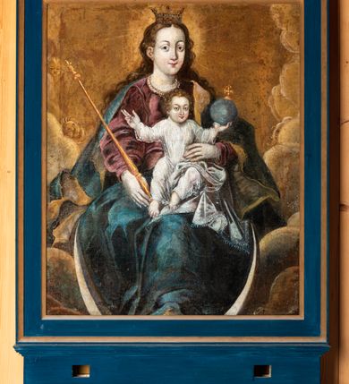 Zdjęcie nr 7: Feretron dwustronny z obrazami w kształcie stojącego prostokąta ujętymi profilowaną ramą, ustawiony na prostopadłościennej podstawie mieszczącej otwory na drążki. Obramienie i podstawa malowane na kolor ciemnogranatowy, miejscowo złocone. Na awersie umieszczono obraz przedstawiający Matkę Boską z Dzieciątkiem ukazaną frontalnie w ujęciu do pasa. Twarz Marii owalna, w trzech czwartych zwrócona w lewo, oczy duże, ciemne, nos długi i prosty, usta niewielkie. Karnacja jasna z delikatnie zaróżowionymi policzkami. Maria ubrana jest w czerwoną suknię przepasaną sznurem. Głowę i ramiona Matki Boskiej okrywa granatowy płaszcz podbity zieloną tkaniną. Jego krańce są lamowane złotą bordiurą wyszywaną perłami oraz zielonymi i czerwonymi kamieniami. Na welon nałożona korona w typie otwartym, zdobiona perłami i kameryzowana. Głowę postaci otacza świetlisty nimb. Swoją prawą dłonią Maria wskazuje na ukazane z prawej strony kompozycji Dzieciątko. Jezus siedzi w trzech czwartych zwrócony ku Marii. Jego głowa jest okrągła, lekko uniesiona, a wzrok skierowany ku górze. Oczy postaci duże, ciemne, nos prosty, długi, usta małe, wąskie. Wokół głowy ukazany świetlisty nimb. Dzieciątko jest ubrane w długą suknię z białej tkaniny, dekorowaną wzorem kwiatowym. Jezus wznosi prawą rękę w geście błogosławieństwa, lewą podtrzymuje księgę leżącą na jego kolanach. W górnej części kompozycji udrapowana czerwono-różowa tkanina z lambrekinem. Tło przedstawienia jednolicie ciemne. Na rewersie obraz Matki Boskiej z Dzieciątkiem trzymającej berło. Maria ukazana w całej postaci, frontalnie w pozycji siedzącej w otoczeniu obłoków z sierpem księżyca pod stopami. Twarz postaci delikatnie zwrócona w prawo, owalna. Oczy duże, szeroko otwarte, nos prosty, długi, usta niewielkie. Włosy Marii długie, brązowe opadające na ramiona i plecy postaci. Na głowie niewielka korona w typie otwartym, wokół niej nimb promienisty. Maria ubrana jest w czerwoną suknię ze złotą lamówką pod szyją oraz obficie fałdowany, niebieski płaszcz podbity złotą tkaniną. Postać w swojej prawej dłoni trzyma złote berło, na lewym kolanie podtrzymuje Dzieciątko. Jezus ukazany frontalnie, w pozycji siedzącej. Wzrok kieruje na widza i szeroko rozkłada ręce. Prawą dłoń składa w geście błogosławieństwa, w lewej podtrzymuje kulę zwieńczoną krzyżem. Jezus jest ubrany w długą, białą suknię, spod której widoczne są bose stopy. Tło przedstawienia złoto-żółte z widocznymi w dolnej części kompozycji obłokami.