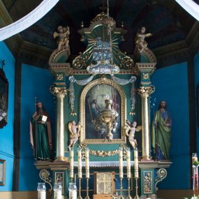 Zdjęcie nr 1: Ołtarz architektoniczny, jednokondygnacyjny, jednoosiowy ze zwieńczeniem. Ołtarz prostopadłościenny, z drewnianą mensą. Antepedium ujęte szerokim obramieniem, pośrodku w polu w kształcie koła złocony monogram imienia Jezus. Retabulum osadzone na zryzalitowanym po bokach cokole, ujętym parą wolutowych impostów. Część środkowa flankowana parą kolumn wspierających niepełne, wyłamujące się ponad nimi, przerwane w partii fryzu belkowanie. Zwieńczenie ujęte parą spływów wolutowych, zamknięte fragmentem gzymsu w postaci półkolistego łuku nadwieszonego, po bokach przerwany, półkolisty przyczółek. Pola cokołu zdobione motywami wici roślinnej. W dolnej części pola środkowego nastawy kwietna girlanda, wyżej, po bokach para aniołków, w górnej partii pośrodku gzymsu kartusz z napisem „OTO BARANEK BOŻY” z podwieszeniem w formie podwiązanej w narożach polach kotary. W partiach fryzu rozety. W zwieńczeniu motyw płaskorzeźbionej Baranka Paschalnego ujętego promienistą glorią. Dolną część spływów wolutowych zdobią liście akantu. Szczyt w formie krzyża osadzonego na ażurowej podstawie w postaci wici akantowej, ujęty parą płomienistych wazonów. Na przerwanym przyczółku para figur siedzących aniołków. Pole części środkowej retabulum w kształcie zbliżonym do kwadratu, zamkniętym półkoliście, ujętym rzeźbioną, złoconą ramą. W środku obraz „Trójcy Świętej”. Po bokach retabulum para rzeźb, po lewej św. Jakub, po prawej św. Józef. Struktura polichromowana w kolorze zielonym i niebieskim, detal architektoniczny złocony i srebrzony.   
