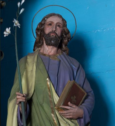 Zdjęcie nr 1: Całopostaciowa, drążona z tyłu figura św. Józefa stojącego na wprost w wyraźnym kontrapoście, na niewysokiej ośmiobocznej podstawie. Nieznacznie przechyloną w lewo głowę charakteryzuje pociągła twarz o delikatnych rysach oraz krótkim, ciemnobrązowym zaroście. Długie, kręcone włosy opadają na plecy. Głowę okala wąska aureola. Święty ubrany jest w fioletową suknię i narzucony na prawe ramię, jasnozielony płaszcz ze złoconym obszyciem. W prawej dłoni trzyma kwiat białej lilii na długim drzewcu, w lewej zamkniętą księgę w brązowej, złoconej oprawie. 

