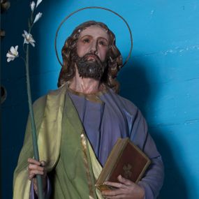 Zdjęcie nr 1: Całopostaciowa, drążona z tyłu figura św. Józefa stojącego na wprost w wyraźnym kontrapoście, na niewysokiej ośmiobocznej podstawie. Nieznacznie przechyloną w lewo głowę charakteryzuje pociągła twarz o delikatnych rysach oraz krótkim, ciemnobrązowym zaroście. Długie, kręcone włosy opadają na plecy. Głowę okala wąska aureola. Święty ubrany jest w fioletową suknię i narzucony na prawe ramię, jasnozielony płaszcz ze złoconym obszyciem. W prawej dłoni trzyma kwiat białej lilii na długim drzewcu, w lewej zamkniętą księgę w brązowej, złoconej oprawie. 

