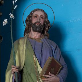 Zdjęcie nr 1: Całopostaciowa, drążona z tyłu figura św. Józefa stojącego na wprost w wyraźnym kontrapoście, na niewysokiej ośmiobocznej podstawie. Nieznacznie przechyloną w lewo głowę charakteryzuje pociągła twarz o delikatnych rysach oraz krótkim, ciemnobrązowym zaroście. Długie, kręcone włosy opadają na plecy. Głowę okala wąska aureola. Święty ubrany jest w fioletową suknię i narzucony na prawe ramię, jasnozielony płaszcz ze złoconym obszyciem. W prawej dłoni trzyma kwiat białej lilii na długim drzewcu, w lewej zamkniętą księgę w brązowej, złoconej oprawie. 

