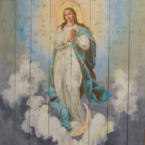 Zdjęcie nr 1: Na jasnoniebieskim tle malowanym w motyw złotych gwiazd wydzielone pole ujęte malowaną ramą w kształcie stojącego prostokąta o bokach wygiętych w łuk wyniesiony. W centrum kompozycji, na tle obłoków przedstawienie Matki Boskiej Niepokalanie Poczętej stojącej na półksiężycu. Maria przedstawiona jako młoda kobieta o jasnych, długich włosach ukazana frontalnie z głową pochyloną lekko w dół i dłońmi złożonymi w geście modlitwy. Postać ubrana jest w obszerną, białą suknię z długimi rękawami i jasnoniebieski płaszcz luźno udrapowany wokół lewego ramienia Marii. Wokół głowy Matki Boskiej znajduje się świetlisty nimb. Kolorystyka malowidła jasna, pastelowa z dominacją różnych odcieni błękitu.


