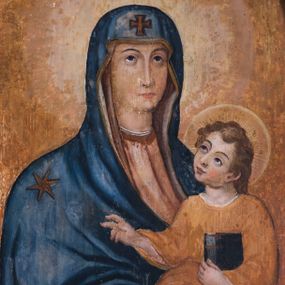 Zdjęcie nr 1: Obraz w kształcie stojącego prostokąta zamknięty półkolistym łukiem nadwieszonym z wizerunkiem Matki Boskiej z Dzieciątkiem. Ukazana w półpostaci Maria jest zwrócona lekko w lewą stronę. Owalną twarz charakteryzują delikatne rysy z cienkimi łukami ciemnych brwi, wzniesionym do góry wzroku, długim, prostym nosem, drobnymi ustami i delikatnie podkreślonym podbródku. Maria ma na sobie jasnoczerwoną suknię oraz ciemnoniebieski płaszcz osłaniający głowę i ramiona, o prawej pole podwiniętej pod lewą rękę, obszyty wąską, złoconą lamówką, z motywem krzyża nad czołem Marii i gwiazdą na jej prawym ramieniu. Na uniesionych na wysokości talii, skrzyżowanych w nadgarstkach rękach trzyma Dzieciątko; prawa dłoń o wyprostowanym palcu wskazującym i środkowym, w lewej trzyma białą chustę. Jezus zwrócony jest w trzech czwartych w prawo. Przechyloną w bok głowę charakteryzuje zaokrąglona twarz o pełnych rysach, z wyraźnymi łukami ciemnych brwi, dużymi skierowanymi na Marię oczami, długim nosem, kształtnymi ustami i wyraźnie zaznaczonym podbródku. Kręcone, zaczesany do tyłu włosy odsłaniają ucho. Jezus ma na sobie długą, ciemnopomarańczową suknię, a na stopach sandały. Lewą ręką podtrzymuje zamkniętą księgę w czarnej oprawie, prawą unosi w geście błogosławieństwa. Głowy postaci okalają nimby.   Tło jest w odcieniach ciemnego pomarańczu i ochry. 