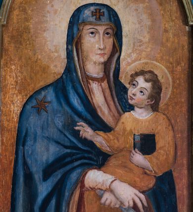 Zdjęcie nr 2: Obraz w kształcie stojącego prostokąta zamknięty półkolistym łukiem nadwieszonym z wizerunkiem Matki Boskiej z Dzieciątkiem. Ukazana w półpostaci Maria jest zwrócona lekko w lewą stronę. Owalną twarz charakteryzują delikatne rysy z cienkimi łukami ciemnych brwi, wzniesionym do góry wzroku, długim, prostym nosem, drobnymi ustami i delikatnie podkreślonym podbródku. Maria ma na sobie jasnoczerwoną suknię oraz ciemnoniebieski płaszcz osłaniający głowę i ramiona, o prawej pole podwiniętej pod lewą rękę, obszyty wąską, złoconą lamówką, z motywem krzyża nad czołem Marii i gwiazdą na jej prawym ramieniu. Na uniesionych na wysokości talii, skrzyżowanych w nadgarstkach rękach trzyma Dzieciątko; prawa dłoń o wyprostowanym palcu wskazującym i środkowym, w lewej trzyma białą chustę. Jezus zwrócony jest w trzech czwartych w prawo. Przechyloną w bok głowę charakteryzuje zaokrąglona twarz o pełnych rysach, z wyraźnymi łukami ciemnych brwi, dużymi skierowanymi na Marię oczami, długim nosem, kształtnymi ustami i wyraźnie zaznaczonym podbródku. Kręcone, zaczesany do tyłu włosy odsłaniają ucho. Jezus ma na sobie długą, ciemnopomarańczową suknię, a na stopach sandały. Lewą ręką podtrzymuje zamkniętą księgę w czarnej oprawie, prawą unosi w geście błogosławieństwa. Głowy postaci okalają nimby.   Tło jest w odcieniach ciemnego pomarańczu i ochry. 