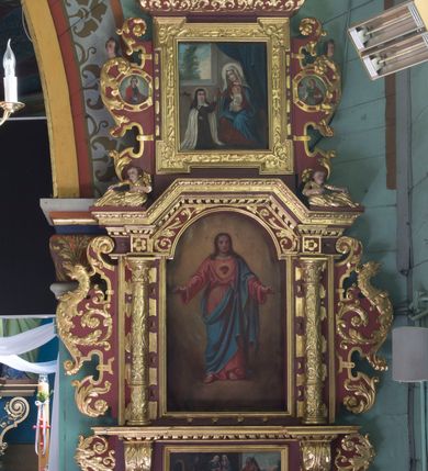 Zdjęcie nr 2: Obraz w kształcie stojącego prostokąta zamkniętego półkolistym łukiem nadwieszonym, z całopostaciowym wizerunkiem Najświętszego Serca Jezusa. Zwrócony na wprost Jezus stoi na obłokach w lekkim kontrapoście. Nieznacznie skierowaną w lewo głowę charakteryzuje owalna twarz o delikatnych rysach z dużymi, wpatrzonymi przed siebie oczami, długim nosem, kształtnymi ustami i krótkim zarostem. Długie, falowane włosy opadają na ramiona. Jezus ubrany jest w długą, czerwoną, przewiązaną w pasie czerwonym sznurem suknię i niebieski płaszcz przerzucony przez lewe ramię i przełożony przez sznur sukni oraz obszyty wąskim, złoconym galonem. Ręce są opuszczone w dół, lekko rozchylone na boki, na dłoniach i stopach widoczne ślady ran. Pośrodku klatki piersiowej gorejące serce ujęte promienistą glorią. Wokół głowy Jezusa ślad po aplikowanym nimbie. Tło w odcieniach ochry. 