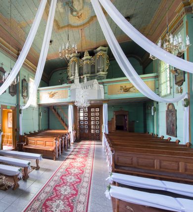 Zdjęcie nr 3: Prospekt organowy o formach architektonicznych, pięcioosiowy, jednokondygnacyjny ze zwieńczeniem. Osie nieparzyste wypukłe; osie skrajne na rzucie trójkąta; oś środkowa niższa na rzucie półkola ujęta w górnej części odwróconymi rogami obfitości. W osiach parzystych niższe płyciny mieszczące mniejsze piszczałki ujęte od góry parą stykających się wolut akantowych. W górnej partii części piszczałkowej osi nieparzystych płaskorzeźbiona dekoracja akantowa. Zwieńczenie utworzone z przełamującego się belkowania. W osi środkowej szczyt w postaci krzyża ujętego parą wolut akantowych. Struktura malowana w odcieniach popielu i jasnej zieleni, ornamenty złocone i srebrzone. Parapet chóru muzycznego w formie pełnej balustrady artykułowanej 4 pilastrami wspierającymi wyłamujący się ponad nimi gzyms wieńczący, wspartej na 4 drewnianych słupach. W polu po lewej stronie polichromowana kompozycja ze skrzypiec zestawionych z gałązką laurową i zwojem papieru nutowego. W płycinie po prawej stronie analogiczna kompozycja z lutnią zamiast skrzypiec. Struktura parapetu polichromowana w pastelowych odcieniach zieleni, błękitu, niebieskiego, brązu i bieli.  
