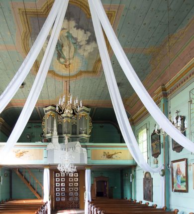 Zdjęcie nr 1: Prospekt organowy o formach architektonicznych, pięcioosiowy, jednokondygnacyjny ze zwieńczeniem. Osie nieparzyste wypukłe; osie skrajne na rzucie trójkąta; oś środkowa niższa na rzucie półkola ujęta w górnej części odwróconymi rogami obfitości. W osiach parzystych niższe płyciny mieszczące mniejsze piszczałki ujęte od góry parą stykających się wolut akantowych. W górnej partii części piszczałkowej osi nieparzystych płaskorzeźbiona dekoracja akantowa. Zwieńczenie utworzone z przełamującego się belkowania. W osi środkowej szczyt w postaci krzyża ujętego parą wolut akantowych. Struktura malowana w odcieniach popielu i jasnej zieleni, ornamenty złocone i srebrzone. Parapet chóru muzycznego w formie pełnej balustrady artykułowanej 4 pilastrami wspierającymi wyłamujący się ponad nimi gzyms wieńczący, wspartej na 4 drewnianych słupach. W polu po lewej stronie polichromowana kompozycja ze skrzypiec zestawionych z gałązką laurową i zwojem papieru nutowego. W płycinie po prawej stronie analogiczna kompozycja z lutnią zamiast skrzypiec. Struktura parapetu polichromowana w pastelowych odcieniach zieleni, błękitu, niebieskiego, brązu i bieli.  