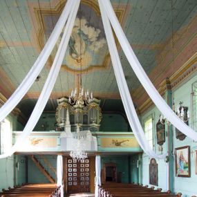 Zdjęcie nr 1: Prospekt organowy o formach architektonicznych, pięcioosiowy, jednokondygnacyjny ze zwieńczeniem. Osie nieparzyste wypukłe; osie skrajne na rzucie trójkąta; oś środkowa niższa na rzucie półkola ujęta w górnej części odwróconymi rogami obfitości. W osiach parzystych niższe płyciny mieszczące mniejsze piszczałki ujęte od góry parą stykających się wolut akantowych. W górnej partii części piszczałkowej osi nieparzystych płaskorzeźbiona dekoracja akantowa. Zwieńczenie utworzone z przełamującego się belkowania. W osi środkowej szczyt w postaci krzyża ujętego parą wolut akantowych. Struktura malowana w odcieniach popielu i jasnej zieleni, ornamenty złocone i srebrzone. Parapet chóru muzycznego w formie pełnej balustrady artykułowanej 4 pilastrami wspierającymi wyłamujący się ponad nimi gzyms wieńczący, wspartej na 4 drewnianych słupach. W polu po lewej stronie polichromowana kompozycja ze skrzypiec zestawionych z gałązką laurową i zwojem papieru nutowego. W płycinie po prawej stronie analogiczna kompozycja z lutnią zamiast skrzypiec. Struktura parapetu polichromowana w pastelowych odcieniach zieleni, błękitu, niebieskiego, brązu i bieli.  