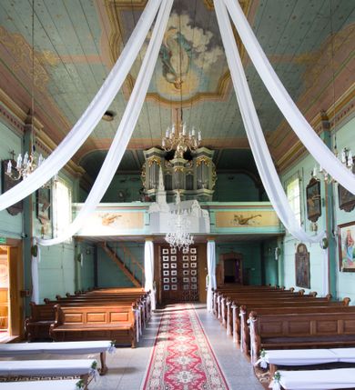 Zdjęcie nr 2: Prospekt organowy o formach architektonicznych, pięcioosiowy, jednokondygnacyjny ze zwieńczeniem. Osie nieparzyste wypukłe; osie skrajne na rzucie trójkąta; oś środkowa niższa na rzucie półkola ujęta w górnej części odwróconymi rogami obfitości. W osiach parzystych niższe płyciny mieszczące mniejsze piszczałki ujęte od góry parą stykających się wolut akantowych. W górnej partii części piszczałkowej osi nieparzystych płaskorzeźbiona dekoracja akantowa. Zwieńczenie utworzone z przełamującego się belkowania. W osi środkowej szczyt w postaci krzyża ujętego parą wolut akantowych. Struktura malowana w odcieniach popielu i jasnej zieleni, ornamenty złocone i srebrzone. Parapet chóru muzycznego w formie pełnej balustrady artykułowanej 4 pilastrami wspierającymi wyłamujący się ponad nimi gzyms wieńczący, wspartej na 4 drewnianych słupach. W polu po lewej stronie polichromowana kompozycja ze skrzypiec zestawionych z gałązką laurową i zwojem papieru nutowego. W płycinie po prawej stronie analogiczna kompozycja z lutnią zamiast skrzypiec. Struktura parapetu polichromowana w pastelowych odcieniach zieleni, błękitu, niebieskiego, brązu i bieli.  