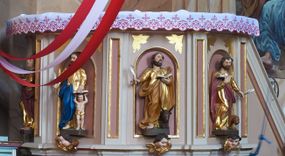 Zdjęcie nr 1: Ambona przyścienna, wisząca, z dostępem w postaci jednobiegowych schodów z pełną balustradą, dostawionych od północy. Kosz na planie ośmioboku, ustawiony na niskim, profilowanym cokole, z podwieszeniem w formie zbliżonej do spłaszczonego stożka, o wklęsło-wypukłych ściankach, zakończonego szyszką. Ścianki ambony wydzielone zwielokrotnionymi pilastrami toskańskimi, z płycinami w partii trzonów, podtrzymującymi przełamujący się nad nimi gzyms tworzący parapet. W polach płyciny w formie stojącego prostokąta zamkniętego łukiem półkolistym z figurami czterech ewangelistów ustawionych na wspornikach w postaci uskrzydlonych główek anielskich. Baldachim na planie ośmioboku, w formie zbliżonej do spłaszczonego stożka, o wklęsło-wypukłych ściankach, o krawędzi obwiedzionej lambrekinem, zakończonego postumentem z figurą Chrystusa w typie Salvator Mundi. Na podniebieniu gołębica Ducha Świętego w glorii promienistej. Struktura polichromowana w odcieniach beżu, z bladoróżowymi detalami i złoconymi profilami. Figury ewangelistów i Chrystusa ścięte z tyłu, ukazane frontalnie, w kontrapostach. Twarze mają pociągłe, o migdałowatych oczach, garbatych nosach i pełnych ustach, okolone są gęstymi, krótkimi brodami i falowanymi włosami opadającymi na ramiona. Postacie ubrane są w złocone tuniki przepasane w talii oraz płaszcze. Ewangeliści trzymają w rękach pióra i otwarte księgi, przy nogach znajdują się ich atrybuty. Chrystus w lewej ręce trzyma jabłko królewskie, prawą błogosławi. 