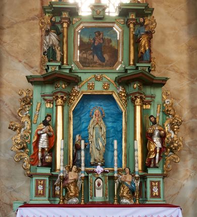 Zdjęcie nr 2: Nastawa ołtarzowa architektoniczna, jednoosiowa, dwukondygnacyjna na cokole z wyodrębnionymi dwoma prostopadłościanami. Ołtarz prostopadłościenny, zwężający się ku dołowi, mensa drewniana. Antepedium marmoryzowane z iluzjonistycznie malowanymi płycinami. Tabernakulum w formie drewnianej skrzynki, półkoliście wybrzuszone od frontu, zakończone profilowanym gzymsem. Drzwiczki o kształcie stojącego prostokąta zamknięte ostrołukiem z malowanym gorejącym sercem, flankowane płaskorzeźbioną winną latoroślą. Tabernakulum ujęte dwiema figurami klęczących na obłokach aniołów. Pierwsza kondygnacja flankowana dwiema parami pilastrów, zewnętrzna o kanelowanych trzonach. Przed wewnętrzną parą stoją dwie kolumny o kapitelach kompozytowych, przed zewnętrzną ustawione są figury św. Stefana i św. Władysława. Podpory dźwigają pełne belkowanie z silnie wysuniętym gzymsem, wyłamane pod kątem w partii kolumn, przerwane pośrodku. W polu centralnym nisza w formie stojącego prostokąta o ściętych górnych narożach ujęta profilowaną ramą, z grupą rzeźbiarską Matki Boskiej z Lourdes i Bernadetą Soubirous. W górnej partii nisza dekorowana zwisami owocowo-kwiatowymi. Pierwsza kondygnacja ujęta uszami utworzonymi z akantu i karbowanej wstęgi. Druga kondygnacja flankowana parą kolumn oraz parą figur św. Marka i św. Mateusza na cokołach. Podpory dźwigają pełne belkowanie z silnie wysuniętym gzymsem, wyłamane na ich osi, przerwane nad polem środkowym. Na belkowaniu dwie figurki aniołków, pośrodku na wsporniku figura Chrystusa w glorii, pośród obłoków. W polu obraz Chrystusa Dobrego Pasterza w formie leżącego prostokąta o ściętych narożach, w ramie. Druga kondygnacja ujęta uszami utworzonymi z akantu. Struktura polichromowana w kolorze jasnozielonym, kolumny, ornamentyka i profile złocone, detal srebrzony. 

