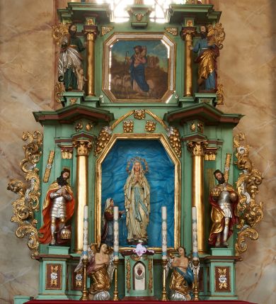 Zdjęcie nr 1: Nastawa ołtarzowa architektoniczna, jednoosiowa, dwukondygnacyjna na cokole z wyodrębnionymi dwoma prostopadłościanami. Ołtarz prostopadłościenny, zwężający się ku dołowi, mensa drewniana. Antepedium marmoryzowane z iluzjonistycznie malowanymi płycinami. Tabernakulum w formie drewnianej skrzynki, półkoliście wybrzuszone od frontu, zakończone profilowanym gzymsem. Drzwiczki o kształcie stojącego prostokąta zamknięte ostrołukiem z malowanym gorejącym sercem, flankowane płaskorzeźbioną winną latoroślą. Tabernakulum ujęte dwiema figurami klęczących na obłokach aniołów. Pierwsza kondygnacja flankowana dwiema parami pilastrów, zewnętrzna o kanelowanych trzonach. Przed wewnętrzną parą stoją dwie kolumny o kapitelach kompozytowych, przed zewnętrzną ustawione są figury św. Stefana i św. Władysława. Podpory dźwigają pełne belkowanie z silnie wysuniętym gzymsem, wyłamane pod kątem w partii kolumn, przerwane pośrodku. W polu centralnym nisza w formie stojącego prostokąta o ściętych górnych narożach ujęta profilowaną ramą, z grupą rzeźbiarską Matki Boskiej z Lourdes i Bernadetą Soubirous. W górnej partii nisza dekorowana zwisami owocowo-kwiatowymi. Pierwsza kondygnacja ujęta uszami utworzonymi z akantu i karbowanej wstęgi. Druga kondygnacja flankowana parą kolumn oraz parą figur św. Marka i św. Mateusza na cokołach. Podpory dźwigają pełne belkowanie z silnie wysuniętym gzymsem, wyłamane na ich osi, przerwane nad polem środkowym. Na belkowaniu dwie figurki aniołków, pośrodku na wsporniku figura Chrystusa w glorii, pośród obłoków. W polu obraz Chrystusa Dobrego Pasterza w formie leżącego prostokąta o ściętych narożach, w ramie. Druga kondygnacja ujęta uszami utworzonymi z akantu. Struktura polichromowana w kolorze jasnozielonym, kolumny, ornamentyka i profile złocone, detal srebrzony. 

