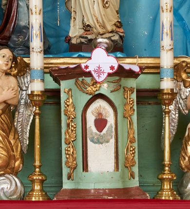 Zdjęcie nr 5: Nastawa ołtarzowa architektoniczna, jednoosiowa, dwukondygnacyjna na cokole z wyodrębnionymi dwoma prostopadłościanami. Ołtarz prostopadłościenny, zwężający się ku dołowi, mensa drewniana. Antepedium marmoryzowane z iluzjonistycznie malowanymi płycinami. Tabernakulum w formie drewnianej skrzynki, półkoliście wybrzuszone od frontu, zakończone profilowanym gzymsem. Drzwiczki o kształcie stojącego prostokąta zamknięte ostrołukiem z malowanym gorejącym sercem, flankowane płaskorzeźbioną winną latoroślą. Tabernakulum ujęte dwiema figurami klęczących na obłokach aniołów. Pierwsza kondygnacja flankowana dwiema parami pilastrów, zewnętrzna o kanelowanych trzonach. Przed wewnętrzną parą stoją dwie kolumny o kapitelach kompozytowych, przed zewnętrzną ustawione są figury św. Stefana i św. Władysława. Podpory dźwigają pełne belkowanie z silnie wysuniętym gzymsem, wyłamane pod kątem w partii kolumn, przerwane pośrodku. W polu centralnym nisza w formie stojącego prostokąta o ściętych górnych narożach ujęta profilowaną ramą, z grupą rzeźbiarską Matki Boskiej z Lourdes i Bernadetą Soubirous. W górnej partii nisza dekorowana zwisami owocowo-kwiatowymi. Pierwsza kondygnacja ujęta uszami utworzonymi z akantu i karbowanej wstęgi. Druga kondygnacja flankowana parą kolumn oraz parą figur św. Marka i św. Mateusza na cokołach. Podpory dźwigają pełne belkowanie z silnie wysuniętym gzymsem, wyłamane na ich osi, przerwane nad polem środkowym. Na belkowaniu dwie figurki aniołków, pośrodku na wsporniku figura Chrystusa w glorii, pośród obłoków. W polu obraz Chrystusa Dobrego Pasterza w formie leżącego prostokąta o ściętych narożach, w ramie. Druga kondygnacja ujęta uszami utworzonymi z akantu. Struktura polichromowana w kolorze jasnozielonym, kolumny, ornamentyka i profile złocone, detal srebrzony. 

