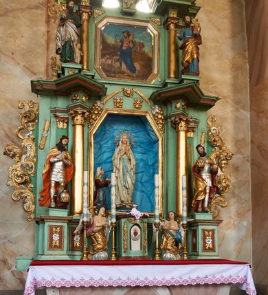 Zdjęcie nr 4: Nastawa ołtarzowa architektoniczna, jednoosiowa, dwukondygnacyjna na cokole z wyodrębnionymi dwoma prostopadłościanami. Ołtarz prostopadłościenny, zwężający się ku dołowi, mensa drewniana. Antepedium marmoryzowane z iluzjonistycznie malowanymi płycinami. Tabernakulum w formie drewnianej skrzynki, półkoliście wybrzuszone od frontu, zakończone profilowanym gzymsem. Drzwiczki o kształcie stojącego prostokąta zamknięte ostrołukiem z malowanym gorejącym sercem, flankowane płaskorzeźbioną winną latoroślą. Tabernakulum ujęte dwiema figurami klęczących na obłokach aniołów. Pierwsza kondygnacja flankowana dwiema parami pilastrów, zewnętrzna o kanelowanych trzonach. Przed wewnętrzną parą stoją dwie kolumny o kapitelach kompozytowych, przed zewnętrzną ustawione są figury św. Stefana i św. Władysława. Podpory dźwigają pełne belkowanie z silnie wysuniętym gzymsem, wyłamane pod kątem w partii kolumn, przerwane pośrodku. W polu centralnym nisza w formie stojącego prostokąta o ściętych górnych narożach ujęta profilowaną ramą, z grupą rzeźbiarską Matki Boskiej z Lourdes i Bernadetą Soubirous. W górnej partii nisza dekorowana zwisami owocowo-kwiatowymi. Pierwsza kondygnacja ujęta uszami utworzonymi z akantu i karbowanej wstęgi. Druga kondygnacja flankowana parą kolumn oraz parą figur św. Marka i św. Mateusza na cokołach. Podpory dźwigają pełne belkowanie z silnie wysuniętym gzymsem, wyłamane na ich osi, przerwane nad polem środkowym. Na belkowaniu dwie figurki aniołków, pośrodku na wsporniku figura Chrystusa w glorii, pośród obłoków. W polu obraz Chrystusa Dobrego Pasterza w formie leżącego prostokąta o ściętych narożach, w ramie. Druga kondygnacja ujęta uszami utworzonymi z akantu. Struktura polichromowana w kolorze jasnozielonym, kolumny, ornamentyka i profile złocone, detal srebrzony. 

