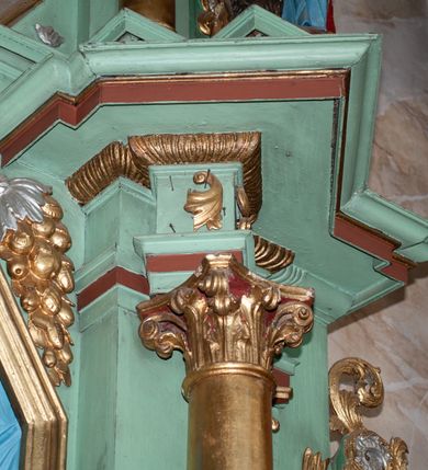 Zdjęcie nr 21: Nastawa ołtarzowa architektoniczna, jednoosiowa, dwukondygnacyjna na cokole z wyodrębnionymi dwoma prostopadłościanami. Ołtarz prostopadłościenny, zwężający się ku dołowi, mensa drewniana. Antepedium marmoryzowane z iluzjonistycznie malowanymi płycinami. Tabernakulum w formie drewnianej skrzynki, półkoliście wybrzuszone od frontu, zakończone profilowanym gzymsem. Drzwiczki o kształcie stojącego prostokąta zamknięte ostrołukiem z malowanym gorejącym sercem, flankowane płaskorzeźbioną winną latoroślą. Tabernakulum ujęte dwiema figurami klęczących na obłokach aniołów. Pierwsza kondygnacja flankowana dwiema parami pilastrów, zewnętrzna o kanelowanych trzonach. Przed wewnętrzną parą stoją dwie kolumny o kapitelach kompozytowych, przed zewnętrzną ustawione są figury św. Stefana i św. Władysława. Podpory dźwigają pełne belkowanie z silnie wysuniętym gzymsem, wyłamane pod kątem w partii kolumn, przerwane pośrodku. W polu centralnym nisza w formie stojącego prostokąta o ściętych górnych narożach ujęta profilowaną ramą, z grupą rzeźbiarską Matki Boskiej z Lourdes i Bernadetą Soubirous. W górnej partii nisza dekorowana zwisami owocowo-kwiatowymi. Pierwsza kondygnacja ujęta uszami utworzonymi z akantu i karbowanej wstęgi. Druga kondygnacja flankowana parą kolumn oraz parą figur św. Marka i św. Mateusza na cokołach. Podpory dźwigają pełne belkowanie z silnie wysuniętym gzymsem, wyłamane na ich osi, przerwane nad polem środkowym. Na belkowaniu dwie figurki aniołków, pośrodku na wsporniku figura Chrystusa w glorii, pośród obłoków. W polu obraz Chrystusa Dobrego Pasterza w formie leżącego prostokąta o ściętych narożach, w ramie. Druga kondygnacja ujęta uszami utworzonymi z akantu. Struktura polichromowana w kolorze jasnozielonym, kolumny, ornamentyka i profile złocone, detal srebrzony. 

