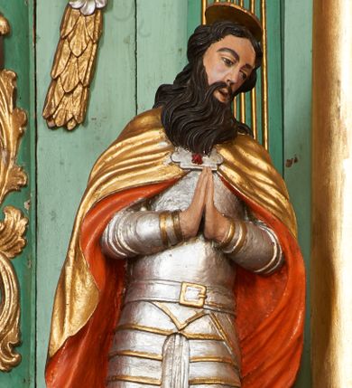 Zdjęcie nr 1: Święty ukazany frontalnie, z głową lekko przechyloną na lewe ramię, dłońmi złożonymi w geście modlitwy. Twarz ma pociągłą, o wąskich oczach, zadartym nosie i otwartych, małych ustach, okoloną długą brodą opadającą na pierś oraz krótkimi, ciemnymi włosami. Nad głową nimb. Ubrany jest w srebrzoną zbroję płytową o złoconych detalach, na ramiona ma narzucony złocony płaszcz o pomarańczowej podszewce, zapięty ozdobną klamrą na piersi. Na lewej stopie świętego leży czerwona poduszka z zamkniętą koroną. Polichromia ciała naturalistyczna.

