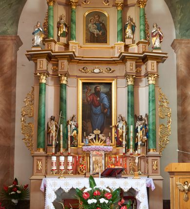 Zdjęcie nr 2: Nastawa ołtarzowa architektoniczna, dwukondygnacyjna ze zwieńczeniem, obie kondygnacje trójosiowe. Ołtarz murowany, prostopadłościenny, mensa z kamiennym portatylem. Antepedium dekorowane malowaną iluzjonistycznie prostokątną płyciną z wypukłymi krótszymi bokami. Na ołtarzu tabernakulum w formie drewnianej skrzynki ujętej kolumienkami podtrzymującymi gzyms. Do niego wbudowana drewniana skrzynka obita metalową blachą, z drzwiczkami w kształcie stojącego prostokąta, ujętego ramą, z wizerunkiem krzyża, winnego grona, kłosów zbóż i kielicha z hostią w polu. Całość flankowana uszami utworzonymi z cęg i kratki. Na tabernakulum tron wystawienia przyjmujący postać glorii promienistej, z parą aniołów unoszącą nad nią koronę zamkniętą. Tron flankowany dwoma klęczącymi aniołkami trzymającymi lichtarze ze świecami. Pierwsza kondygnacja na dwustrefowym cokole, w górnej partii z wyodrębnionymi prostopadłościanami, dekorowanymi płycinami z ornamentem roślinnym. Osie wydzielone czterema kolumnami o kapitelach kompozytowych, dźwigających pełne belkowanie z silnie wysuniętym gzymsem, wyłamane na ich osi oraz ustawione pod kątem na zewnątrz. Fryz dekorowany medalionem z monogramem IHS, uskrzydlonymi główkami anielskimi i ornamentem roślinnym. W polu środkowym wnęka w formie stojącego prostokąta, ujęta profilowaną ramą, z obrazem św. Jakuba. Wnęka flankowana figurami św. Katarzyny Aleksandryjskiej i św. Barbary ustawionymi na cokołach. Na osiach bocznych rzeźby św. Jana Chrzciciela i św. Andrzeja na cokołach. Pierwsza kondygnacja flankowana uszami utworzonymi z wici roślinnej i kratki. Druga kondygnacja na cokole z wyodrębnionymi prostopadłościanami, dekorowanymi płycinami z ornamentem roślinnym. Osie wydzielone czterema kolumnami o kapitelach kompozytowych, dźwigającymi pełne belkowanie, wyłamane na ich osi. Wewnętrzna para zwrócona pod kątem do środka, para skrajna na zewnątrz. Fryz dekorowany uskrzydlonymi główkami anielskimi. W polu obraz św. Józefa z Dzieciątkiem w formie stojącego prostokąta zamkniętego łukiem odcinkowym, ujęty profilowaną ramą. Na osiach bocznych ustawione figury niezidentyfikowanej świętej i św. Jadwigi (?). Na skraju belkowania pierwszej kondygnacji umiejscowione rzeźby Marii i św. Jana. Druga kondygnacja flankowana uszami utworzonymi z wici roślinnej. Zwieńczenie w kształcie zbliżonym do leżącego prostokąta, o wklęsłych bokach, zamkniętego łukiem odcinkowym nadwieszonym. W polu grupa rzeźbiarska Koronacji Marii, w której postacie unoszą się na obłokach, nad nimi zaś znajduje się gołębica Ducha Świętego w glorii. Na belkowaniu drugiej kondygnacji ustawione dwa klęczące na obłokach aniołki oraz figury św. Stefana i św. Władysława. Struktura polichromowana w kolorze beżowym, z bladoróżowymi detalami; kolumny malowane na sposób imitujący marmoryzacje w kolorze zielonym; profile i ornamentyka złocone. 

