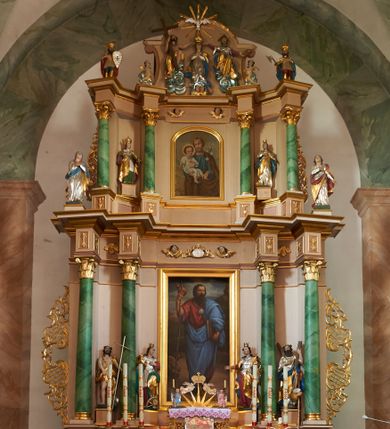 Zdjęcie nr 1: Nastawa ołtarzowa architektoniczna, dwukondygnacyjna ze zwieńczeniem, obie kondygnacje trójosiowe. Ołtarz murowany, prostopadłościenny, mensa z kamiennym portatylem. Antepedium dekorowane malowaną iluzjonistycznie prostokątną płyciną z wypukłymi krótszymi bokami. Na ołtarzu tabernakulum w formie drewnianej skrzynki ujętej kolumienkami podtrzymującymi gzyms. Do niego wbudowana drewniana skrzynka obita metalową blachą, z drzwiczkami w kształcie stojącego prostokąta, ujętego ramą, z wizerunkiem krzyża, winnego grona, kłosów zbóż i kielicha z hostią w polu. Całość flankowana uszami utworzonymi z cęg i kratki. Na tabernakulum tron wystawienia przyjmujący postać glorii promienistej, z parą aniołów unoszącą nad nią koronę zamkniętą. Tron flankowany dwoma klęczącymi aniołkami trzymającymi lichtarze ze świecami. Pierwsza kondygnacja na dwustrefowym cokole, w górnej partii z wyodrębnionymi prostopadłościanami, dekorowanymi płycinami z ornamentem roślinnym. Osie wydzielone czterema kolumnami o kapitelach kompozytowych, dźwigających pełne belkowanie z silnie wysuniętym gzymsem, wyłamane na ich osi oraz ustawione pod kątem na zewnątrz. Fryz dekorowany medalionem z monogramem IHS, uskrzydlonymi główkami anielskimi i ornamentem roślinnym. W polu środkowym wnęka w formie stojącego prostokąta, ujęta profilowaną ramą, z obrazem św. Jakuba. Wnęka flankowana figurami św. Katarzyny Aleksandryjskiej i św. Barbary ustawionymi na cokołach. Na osiach bocznych rzeźby św. Jana Chrzciciela i św. Andrzeja na cokołach. Pierwsza kondygnacja flankowana uszami utworzonymi z wici roślinnej i kratki. Druga kondygnacja na cokole z wyodrębnionymi prostopadłościanami, dekorowanymi płycinami z ornamentem roślinnym. Osie wydzielone czterema kolumnami o kapitelach kompozytowych, dźwigającymi pełne belkowanie, wyłamane na ich osi. Wewnętrzna para zwrócona pod kątem do środka, para skrajna na zewnątrz. Fryz dekorowany uskrzydlonymi główkami anielskimi. W polu obraz św. Józefa z Dzieciątkiem w formie stojącego prostokąta zamkniętego łukiem odcinkowym, ujęty profilowaną ramą. Na osiach bocznych ustawione figury niezidentyfikowanej świętej i św. Jadwigi (?). Na skraju belkowania pierwszej kondygnacji umiejscowione rzeźby Marii i św. Jana. Druga kondygnacja flankowana uszami utworzonymi z wici roślinnej. Zwieńczenie w kształcie zbliżonym do leżącego prostokąta, o wklęsłych bokach, zamkniętego łukiem odcinkowym nadwieszonym. W polu grupa rzeźbiarska Koronacji Marii, w której postacie unoszą się na obłokach, nad nimi zaś znajduje się gołębica Ducha Świętego w glorii. Na belkowaniu drugiej kondygnacji ustawione dwa klęczące na obłokach aniołki oraz figury św. Stefana i św. Władysława. Struktura polichromowana w kolorze beżowym, z bladoróżowymi detalami; kolumny malowane na sposób imitujący marmoryzacje w kolorze zielonym; profile i ornamentyka złocone. 

