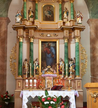 Zdjęcie nr 3: Nastawa ołtarzowa architektoniczna, dwukondygnacyjna ze zwieńczeniem, obie kondygnacje trójosiowe. Ołtarz murowany, prostopadłościenny, mensa z kamiennym portatylem. Antepedium dekorowane malowaną iluzjonistycznie prostokątną płyciną z wypukłymi krótszymi bokami. Na ołtarzu tabernakulum w formie drewnianej skrzynki ujętej kolumienkami podtrzymującymi gzyms. Do niego wbudowana drewniana skrzynka obita metalową blachą, z drzwiczkami w kształcie stojącego prostokąta, ujętego ramą, z wizerunkiem krzyża, winnego grona, kłosów zbóż i kielicha z hostią w polu. Całość flankowana uszami utworzonymi z cęg i kratki. Na tabernakulum tron wystawienia przyjmujący postać glorii promienistej, z parą aniołów unoszącą nad nią koronę zamkniętą. Tron flankowany dwoma klęczącymi aniołkami trzymającymi lichtarze ze świecami. Pierwsza kondygnacja na dwustrefowym cokole, w górnej partii z wyodrębnionymi prostopadłościanami, dekorowanymi płycinami z ornamentem roślinnym. Osie wydzielone czterema kolumnami o kapitelach kompozytowych, dźwigających pełne belkowanie z silnie wysuniętym gzymsem, wyłamane na ich osi oraz ustawione pod kątem na zewnątrz. Fryz dekorowany medalionem z monogramem IHS, uskrzydlonymi główkami anielskimi i ornamentem roślinnym. W polu środkowym wnęka w formie stojącego prostokąta, ujęta profilowaną ramą, z obrazem św. Jakuba. Wnęka flankowana figurami św. Katarzyny Aleksandryjskiej i św. Barbary ustawionymi na cokołach. Na osiach bocznych rzeźby św. Jana Chrzciciela i św. Andrzeja na cokołach. Pierwsza kondygnacja flankowana uszami utworzonymi z wici roślinnej i kratki. Druga kondygnacja na cokole z wyodrębnionymi prostopadłościanami, dekorowanymi płycinami z ornamentem roślinnym. Osie wydzielone czterema kolumnami o kapitelach kompozytowych, dźwigającymi pełne belkowanie, wyłamane na ich osi. Wewnętrzna para zwrócona pod kątem do środka, para skrajna na zewnątrz. Fryz dekorowany uskrzydlonymi główkami anielskimi. W polu obraz św. Józefa z Dzieciątkiem w formie stojącego prostokąta zamkniętego łukiem odcinkowym, ujęty profilowaną ramą. Na osiach bocznych ustawione figury niezidentyfikowanej świętej i św. Jadwigi (?). Na skraju belkowania pierwszej kondygnacji umiejscowione rzeźby Marii i św. Jana. Druga kondygnacja flankowana uszami utworzonymi z wici roślinnej. Zwieńczenie w kształcie zbliżonym do leżącego prostokąta, o wklęsłych bokach, zamkniętego łukiem odcinkowym nadwieszonym. W polu grupa rzeźbiarska Koronacji Marii, w której postacie unoszą się na obłokach, nad nimi zaś znajduje się gołębica Ducha Świętego w glorii. Na belkowaniu drugiej kondygnacji ustawione dwa klęczące na obłokach aniołki oraz figury św. Stefana i św. Władysława. Struktura polichromowana w kolorze beżowym, z bladoróżowymi detalami; kolumny malowane na sposób imitujący marmoryzacje w kolorze zielonym; profile i ornamentyka złocone. 

