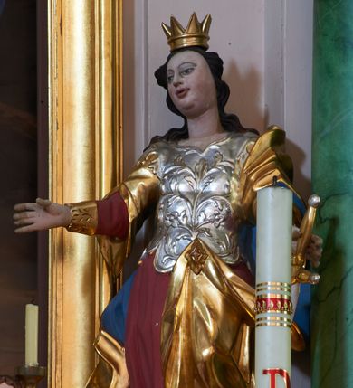 Zdjęcie nr 1: Rzeźba drążona, ustawiona na podstawie na planie kwadratu. Święta ukazana frontalnie, z głową lekko przechyloną w prawo, w kontrapoście, obie ręce wyciągnięte na boki, w lewej trzyma miecz skierowany ostrzem w dół. Twarz ma pełną, z wąskimi, migdałowatymi oczami, niewielkim nosem i lekko otwartymi, pełnymi ustami. Włosy ma ciemnobrązowe, falowane, opadające na ramiona. Na głowie korona otwarta. Święta ubrana w czerwono-różową suknię, ze złoconymi, szerokimi rękawami, srebrzony gorset dekorowany płaskorzeźbionym wzorem roślinnym oraz złocony płaszcz z niebieską podszewką, przerzucony przez lewe ramię, upięty broszką na lewym biodrze. Polichromia w partiach ciała naturalistyczna. 