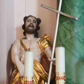 Zdjęcie nr 1: Rzeźba ścięta z tyłu, ustawiona na podstawie na planie kwadratu. Święty ukazany frontalnie, w kontrapoście. W lewej, wyciągniętej do przodu ręce trzyma laskę zakończoną krzyżem, prawą podtrzymuje z przodu płaszcz. Twarz ma owalną, o dużych, migdałowatych oczach, zadartym nosie i wąskich, otwartych ustach, okoloną krótką, silnie kręconą brodą oraz falowanymi włosami sięgającymi ramion. Ubrany jest w melotę zarzuconą na prawe ramię i zawiniętą wokół bioder, odsłaniającą klatkę piersiową i lewą nogę. Przy lewej nodze świętego srebrzony baranek. Polichromia ciała naturalistyczna. 

