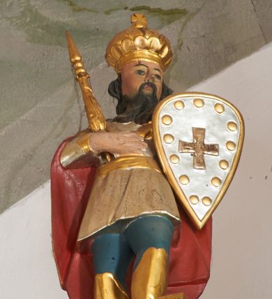 Zdjęcie nr 1: Rzeźba pełna, ukazana frontalnie, z głową skierowaną w lewo, w kontrapoście, prawą dłoń kładzie na piersi, trzyma w niej berło, w lewej zaś tarczę z krzyżem. Twarz ma kwadratową, o migdałowatych oczach, małym nosie i ustach, okoloną długą, ciemną brodą oraz falowanymi włosami. Ubrany jest w niebieskie spodnie i wysokie, złocone buty, krótką, srebrzoną tunikę, przewiązaną w pasie złoconą szarfą, na ramiona ma narzucony złocony płaszcz z czerwoną podszewką. Na głowie ma złoconą, zamkniętą koronę zwieńczoną krzyżem. Polichromia naturalistyczna w partiach ciała.