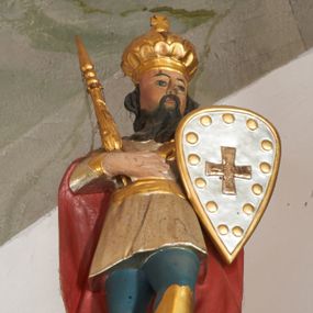 Zdjęcie nr 1: Rzeźba pełna, ukazana frontalnie, z głową skierowaną w lewo, w kontrapoście, prawą dłoń kładzie na piersi, trzyma w niej berło, w lewej zaś tarczę z krzyżem. Twarz ma kwadratową, o migdałowatych oczach, małym nosie i ustach, okoloną długą, ciemną brodą oraz falowanymi włosami. Ubrany jest w niebieskie spodnie i wysokie, złocone buty, krótką, srebrzoną tunikę, przewiązaną w pasie złoconą szarfą, na ramiona ma narzucony złocony płaszcz z czerwoną podszewką. Na głowie ma złoconą, zamkniętą koronę zwieńczoną krzyżem. Polichromia naturalistyczna w partiach ciała.