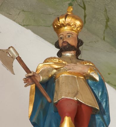 Zdjęcie nr 1: Rzeźba pełna. Święty ukazany frontalnie, z głową skierowaną w prawo, w kontrapoście. Lewą rękę ma złożoną na piersi, w prawej odchylonej od tułowia trzyma topór. Twarz ma kwadratową, o dużych, migdałowatych oczach, małym nosie i ustach, okoloną krótką brodą i falowanymi włosami sięgającymi ramion. Ubrany jest w czerwone spodnie oraz wysokie, złote buty, w krótką, srebrzoną tunikę, przewiązaną w pasie złotą szarfą. Na ramiona ma narzucony złocony, rozłożysty płaszcz z błękitną podszewką, spięty pod szyją. Na głowie ma złoconą koronę zamkniętą zwieńczoną krzyżem. Polichromia naturalistyczna w partiach ciała.