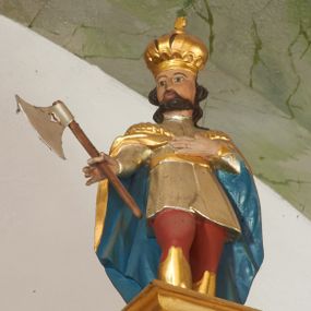 Zdjęcie nr 1: Rzeźba pełna. Święty ukazany frontalnie, z głową skierowaną w prawo, w kontrapoście. Lewą rękę ma złożoną na piersi, w prawej odchylonej od tułowia trzyma topór. Twarz ma kwadratową, o dużych, migdałowatych oczach, małym nosie i ustach, okoloną krótką brodą i falowanymi włosami sięgającymi ramion. Ubrany jest w czerwone spodnie oraz wysokie, złote buty, w krótką, srebrzoną tunikę, przewiązaną w pasie złotą szarfą. Na ramiona ma narzucony złocony, rozłożysty płaszcz z błękitną podszewką, spięty pod szyją. Na głowie ma złoconą koronę zamkniętą zwieńczoną krzyżem. Polichromia naturalistyczna w partiach ciała.