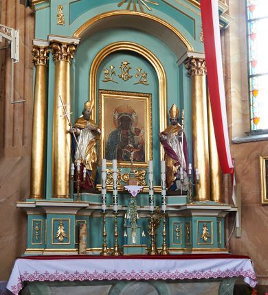 Zdjęcie nr 4: Nastawa ołtarzowa architektoniczna, jednoosiowa, jednokondygnacyjna, na cokole z wyodrębnionymi zwielokrotnionymi prostopadłościanami. Ołtarz murowany, prostopadłościenny, rozszerzający się ku górze. Mensa kamienna; antepedium marmoryzowane z iluzjonistycznie malowaną płyciną z medalionem. Cokół dekorowany płycinami z ornamentem roślinnym i kampanulami. Nastawa ujęta dwiema parami kolumn w układzie schodkowym. Wewnętrzna para podtrzymuje łuk odcinkowy, wszystkie podpory zaś trójkątny szczyt zamknięty profilowanym gzymsem z kostkowaniem, dekorowany wicią roślinną, całość zwieńczona krzyżem. Pole środkowe tworzy nisza w formie stojącego prostokąta zamkniętego łukiem odcinkowym, wewnątrz niej mniejsza płycina o kształcie stojącego prostokąta zamkniętego łukiem półkolistym, ujęta profilowaną ramą, z mniejszym obrazem Matki Boskiej Częstochowskiej, w osobnej, profilowanej ramie. Nad obrazem monogram maryjny flankowany gałązkami lilii, pod nim ornament roślinny. Po bokach wizerunku znajdują się figury św. Stanisława i św. Wojciecha ustawione na niskich cokołach. W przestrzeni szczytu wnęka o fantazyjnym kształcie z okiem Opatrzności w glorii promienistej. Struktura polichromowana w kolorze jasnozielonym, płyciny na zielono; ornamentyka, profile i kolumny złocone.