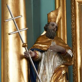 Zdjęcie nr 1: Rzeźba pełna, ustawiona na nieregularnej podstawie. Święty ukazany frontalnie, z głową przechyloną w lewo, w kontrapoście, o delikatnie przegiętej sylwetce. Lewą rękę ma ugiętą, uniesioną na wysokość piersi, w prawej trzyma laskę zakończoną krzyżem. Twarz ma pociągłą, o migdałowatych oczach, małym nosie i pełnych utach, okoloną brązową brodą i skręconymi, krótkimi włosami. Postać ubrana jest w długą, czerwoną albę, srebrzoną rokietę ze złoconym brzegiem oraz złoconą kapę z granatową podszewką, zapiętą klamrą na piersi i zawiniętą na lewej nodze. Na głowie ma złoconą infułę. Polichromia naturalistyczna w partiach ciała.