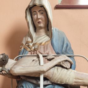 Zdjęcie nr 1: Matka Boska siedząca na tronie z płaskorzeźbioną dekoracją w formie maswerku, na jej kolanach horyzontalnie ułożone, martwe ciało Chrystusa. Dojrzała kobieta w bladoróżowej sukni i błękitnym płaszczu układającym się po bokach w kaskady fał. Poomiędzy nimi szaty uformowane w kształt litery V, na głowie biała chusta wykończona złotą lamówką. Ciało Chrystusa wychudzone z zaznaczonymi śladami męki, głowa w koronie cierniowej lekko odchylona do tyłu, włosy układające się w spiralne loki. Ręce złożone na wysokości bioder. Biodra ma owiniete jasnym perizonium.