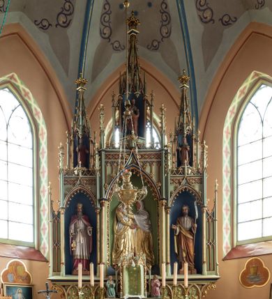 Zdjęcie nr 2: Ołtarz przyścienny, architektoniczny, trójosiowy, jednokondygnacyjny ze zwieńczeniem. Mensa skrzyniowa, prostopadłościenna. Na niej dwukondygnacyjne tabernakulum. W dolnej partii dekorowane postacia Baranka Apokaliptycznego drzwiczki ujęte otrołukowymi niszami wypełnionymi pękami kłosó. W drugiej kondygnacji tron wystawienia z niszą zdobioną rozetami i monogramem „IHS”, zwieńczoną nadwieszonymi łukami w ośli grzbiet z pinaklami i kwiatonami i ujętą parą klęczących aniołów. Predella wysoka, dekorowana fryzem arkadkowym, ostrołukowym, wypełnionym fragmentami wili winnej latorośli. W pierwszej kondygnacji retabulum trzy nisze prostokątne zamknięte od góry wimpergą na tle szczytu, ujete pinaklami wspartymi na służkach. Środkowa nisza wyższa i szersza od bocznych, rama dekorowana wyschniętą wicią roślinną, wszystkie zdobione ażurowym ornamentem ostrołukowym i żabkami; szczyty dekoruje fryz z rombami wypełnionymi czworoliśćmi.  Boczne nisze zwieńczone ustawionymi skośnie ażurowymi kapliczkami z pinaklami, zdobionymi żabkami i kwiatonami z rzeźbą mężczyzny z wiosłem po lewej i kobiety z lilią po prawej stronie. W środkowej niszy kondygnacji płaskorzeźbiona scena Nawiedzenia Najświętszej Marii Panny, w bocznych postać starego mężczyzny z kadzielnicą i św. Jan Chrzciciel. Kondygnacja ujęta uszakami utworzonymi z przypór z blendami i pinaklami. W zwieńczeniu ażurowa kapliczka powtarzająca kształt kapliczek wieńczących osie boczne pierwszej kondygnacji z niszą, w której figura św. Józefa z Dzieciątkiem. 
Struktura jasnozielona, nisze niebieskie, fragmenty dekoracji czerwone i niebieskie, detale złocone. 
