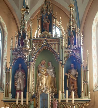 Zdjęcie nr 1: Ołtarz przyścienny, architektoniczny, trójosiowy, jednokondygnacyjny ze zwieńczeniem. Mensa skrzyniowa, prostopadłościenna. Na niej dwukondygnacyjne tabernakulum. W dolnej partii dekorowane postacia Baranka Apokaliptycznego drzwiczki ujęte otrołukowymi niszami wypełnionymi pękami kłosó. W drugiej kondygnacji tron wystawienia z niszą zdobioną rozetami i monogramem „IHS”, zwieńczoną nadwieszonymi łukami w ośli grzbiet z pinaklami i kwiatonami i ujętą parą klęczących aniołów. Predella wysoka, dekorowana fryzem arkadkowym, ostrołukowym, wypełnionym fragmentami wili winnej latorośli. W pierwszej kondygnacji retabulum trzy nisze prostokątne zamknięte od góry wimpergą na tle szczytu, ujete pinaklami wspartymi na służkach. Środkowa nisza wyższa i szersza od bocznych, rama dekorowana wyschniętą wicią roślinną, wszystkie zdobione ażurowym ornamentem ostrołukowym i żabkami; szczyty dekoruje fryz z rombami wypełnionymi czworoliśćmi.  Boczne nisze zwieńczone ustawionymi skośnie ażurowymi kapliczkami z pinaklami, zdobionymi żabkami i kwiatonami z rzeźbą mężczyzny z wiosłem po lewej i kobiety z lilią po prawej stronie. W środkowej niszy kondygnacji płaskorzeźbiona scena Nawiedzenia Najświętszej Marii Panny, w bocznych postać starego mężczyzny z kadzielnicą i św. Jan Chrzciciel. Kondygnacja ujęta uszakami utworzonymi z przypór z blendami i pinaklami. W zwieńczeniu ażurowa kapliczka powtarzająca kształt kapliczek wieńczących osie boczne pierwszej kondygnacji z niszą, w której figura św. Józefa z Dzieciątkiem. 
Struktura jasnozielona, nisze niebieskie, fragmenty dekoracji czerwone i niebieskie, detale złocone. 
