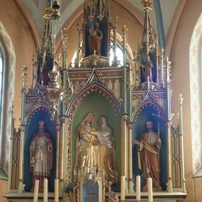 Zdjęcie nr 1: Ołtarz przyścienny, architektoniczny, trójosiowy, jednokondygnacyjny ze zwieńczeniem. Mensa skrzyniowa, prostopadłościenna. Na niej dwukondygnacyjne tabernakulum. W dolnej partii dekorowane postacia Baranka Apokaliptycznego drzwiczki ujęte otrołukowymi niszami wypełnionymi pękami kłosó. W drugiej kondygnacji tron wystawienia z niszą zdobioną rozetami i monogramem „IHS”, zwieńczoną nadwieszonymi łukami w ośli grzbiet z pinaklami i kwiatonami i ujętą parą klęczących aniołów. Predella wysoka, dekorowana fryzem arkadkowym, ostrołukowym, wypełnionym fragmentami wili winnej latorośli. W pierwszej kondygnacji retabulum trzy nisze prostokątne zamknięte od góry wimpergą na tle szczytu, ujete pinaklami wspartymi na służkach. Środkowa nisza wyższa i szersza od bocznych, rama dekorowana wyschniętą wicią roślinną, wszystkie zdobione ażurowym ornamentem ostrołukowym i żabkami; szczyty dekoruje fryz z rombami wypełnionymi czworoliśćmi.  Boczne nisze zwieńczone ustawionymi skośnie ażurowymi kapliczkami z pinaklami, zdobionymi żabkami i kwiatonami z rzeźbą mężczyzny z wiosłem po lewej i kobiety z lilią po prawej stronie. W środkowej niszy kondygnacji płaskorzeźbiona scena Nawiedzenia Najświętszej Marii Panny, w bocznych postać starego mężczyzny z kadzielnicą i św. Jan Chrzciciel. Kondygnacja ujęta uszakami utworzonymi z przypór z blendami i pinaklami. W zwieńczeniu ażurowa kapliczka powtarzająca kształt kapliczek wieńczących osie boczne pierwszej kondygnacji z niszą, w której figura św. Józefa z Dzieciątkiem. 
Struktura jasnozielona, nisze niebieskie, fragmenty dekoracji czerwone i niebieskie, detale złocone. 
