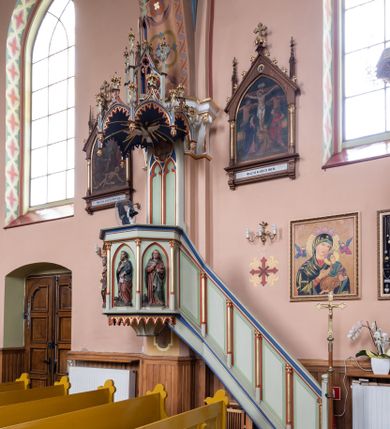 Zdjęcie nr 1: Ambona wisząca, przyścienna składająca się z kosza, zaplecka, baldachimu i schodów z balustradą. Kosz na planie wieloboku, podzielony na pola kolumienkami podtrzymującymi belkowanie, którego gzyms stanowi parapet. W polach płyciny w formie stojącego prostokąta zamkniętego łukiem ostrym. W płycinach całopostaciowe figury ewangelistów – od strony schodów – św. Jan, św. Marek, św. Łukasz i św. Mateusz. Każdy z nich ubrany w długą suknię, z narzuconym płaszczem, trzyma w rękach księgę lub zwój i ma (prócz Łukasza) przy nodze właściwy atrybut. Rzeźby są wolnostojące, na cokołach z podpisami. Wzdłuż ramy dolnej ażurowy ornament maswerkowy. Podstawa zwęża się ku dołowi, ścięta płasko. Zaplecek w kształcie stojącego prostokąta, wypełniony płyciną zamkniętą łukiem ostrym, ze zdwojonym łukiem i rozetą z czworoliściem.  Rozbudowany baldachim powtarza kształt kosza, składa się z arkad ujmujących zwieńczenie w formie kapliczki. Arkady od wewnątrz zdobi maswerkowy fryz, a wieńczą trójkątne, ażurowe szczyty z żabkami i kwiatonami. Wieńcząca kapliczka dwukondygnacyjna, z pinaklami, żabkami i kwiatonami; najwyższe pinakiel zakończony krzyżem. Struktura jasnozielona, niektóre elementy niebieskie lub czerwone, profile i ornamenty złocone.