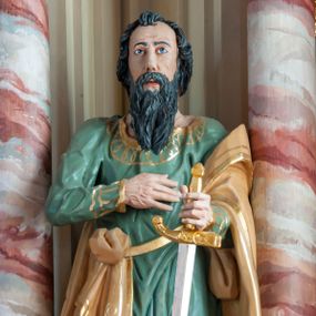 Zdjęcie nr 1: Rzeźba pełna, ustawiona na prostopadłościennym cokole. Figura ukazana w całej postaci, zwrócona frontalnie, w delikatnym kontrapoście, z lewym kolanem zgiętym. Głowa ustawiona na wprost, twarz podłużna, szczupła, okolona gęstym zarostem; wzrok zwrócony przed siebie. Ciemne włosy formują lok nad czołem i opadają na kark zasłaniając uszy, wąsy są szerokie, broda dzieli się w dwa pukle. Święty prawą, zgiętą rękę przyciska do piersi, w wyciągniętej przed siebie lewej trzyma rękojeść opartego o ziemię miecza. Apostoł jest ubrany zieloną w suknię sięgającą ziemi, wykończoną przy krawędziach złotym ornamentem geometrycznym; tkanina łamie się w sztywne, drobne fałdki. Beżowy, dekorowany złotym ornamentem roślinnym płaszcz otacza lewą rękę i jest zatknięty za pasem przy prawym biodrze. Polichromia naturalistyczna w odsłoniętych partiach ciała, miecz złocony i srebrzony. 