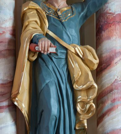 Zdjęcie nr 1: Rzeźba pełna, ustawiona na prostopadłościennym cokole. Figura ukazana w całej postaci, zwrócona frontalnie, w kontrapoście, z prawą nogą zgiętą. Głowa przechylona na lewe ramię, uniesiona; twarz prostokątna, okolona zarostem; wzrok uniesiony. Siwiejące włosy formują lok nad czołem, wąsy dzielą się na równoległe pasemka, broda skręcona w niewielkie loki. Święty prawą ręką dociska do ciała zamkniętą księgę, w lewej, uniesionej trzyma dwa klucze. Apostoł jest ubrany w niebieską suknię sięgającą ziemi, wykończoną przy krawędziach złotym ornamentem; beżowy, lamowany złotem płaszcz otacza prawą rękę i jest zatknięty za pasem przy lewym biodrze, opada ku ziemi dekoracyjnymi fałdami. Polichromia naturalistyczna w odsłoniętych partiach ciała, księga czerwona, o białych kartach, jeden klucz złocony, drugi srebrzony. 