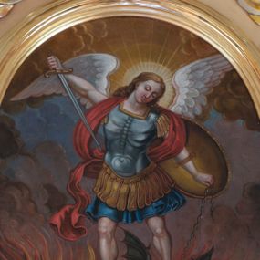Zdjęcie nr 1: Obraz w kształcie stojącego owalu w profilowanej, złoconej ramie z przedstawieniem św. Michała Archanioła walczącego z szatanem. W centrum kompozycji archanioł w momencie ataku wznosi się powyżej szatana na rozpostartych, złożonych z piór skrzydłach, opierając na nim obie stopy. W prawej ręce trzyma skierowany ostrzem w stronę diabła miecz, w lewej łańcuch, którym ten jest spętany, ma na niej również założoną tarczę. Archanioł ma małą, owalną głowę z półprzymkniętymi oczami i wąskim nosem, jasne, długie, falowane włosy opadają mu na plecy; wokół głowy świętego nimb. Jest ubrany w strój żołnierza rzymskiego: niebieski pancerz z naramiennikami założony na granatową tunikę i sandały; wokół ramion i za plecami ma czerwoną szarfę, której koniec rozwiewa się z lewej strony. W dolnej partii obrazu szatan zobrazowany został jako zielonobrązowy, podobny do człowieka stwór, obiema rękami trzymający trójząb. Wokół niego strzelają w górę pomarańczowożółte płomienie. Tło utrzymane w ciepłej tonacji, wypełniające je dołem brunatne chmury przechodzą wyżej w niebieskie i ciemnożółte. 