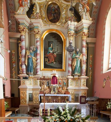 Zdjęcie nr 2: Nastawa ołtarzowa architektoniczna, jednoosiowa, jednokondygnacyjna ze zwieńczeniem, na podwójnym cokole. Ołtarz drewniany, prostopadłościenny; mensa drewniana z kamiennym portatylem. Antepedium podzielone na trzy pola czterema półkolumnami o stylizowanych kapitelach. W polach płyciny; w środkowej romb z płaskorzeźbionym kielichem z hostią; w zewnętrznych winne grona z kłosami zbóż.Tabernakulum w formie drewnianej skrzynki obitej blachą. Drzwiczki w kształcie stojącego prostokąta z aplikowaną, odlewaną plakietką ze sceną modlitwy Chrystusa w Ogrójcu, w narożach aplikowane uskrzydlone główki anielskie, całość w opasce dekorowanej różami. Tabernakulum w drewnianej obudowie, ściana frontowa flankowana parą kolumn. Tron wystawienia w formie niszy ujętej kolumienkami z łukiem o fantazyjnym wykroju. Całość zwieńczona rzeźbioną figurką Baranka Eucharystycznego leżącego na księdze. Po bokach tabernakulum stoją dwie pary nisz na postumentach z figurami czterech ewangelistów. Kondygnacja nastawy ujęta dwiema parami kolumn o kapitelach kompozytowych, stojących na tle zwielokrotnionych pilastrów. Podpory dźwigają fragmenty wyłamanego belkowania, zewnętrzna para również przerwany, wklęsło-wypukły przyczółek. Cokoły ustawione delikatnie pod kątem, zwrócone na zewnątrz. Na gzymsie wewnętrznych podpór niewielkie figurki puttów; na przyczółkach figury siedzących aniołów ubranych w długie suknie, okryte czerwonymi płaszczami. Między kolumnami na wspornikach figury św. Piotra i św. Pawła. W polu środkowym obraz św. Aleksego w profilowanej ramie w kształcie stojącego prostokąta zamkniętego łukiem półkolistym nadwieszonym. Zwieńczenie w formie leżącego prostokąta, ujętego masywnymi spływami wolutowymi, zamkniętego przeciwstawnie zwróconymi esownicami. W polu obraz św. Michała Archanioła w profilowanej ramie w formie stojącego owalu. Dolne partie cokołu dekorowane płaskorzeźbionym, stylizowanym akantem o układzie geometrycznym; wyższe z ornamentem w płycinach. Kondygnacja ujęta uszakami utworzonymi z karbowanej wstęgi przeplatającej się z ornamentem roślinnym. Woluty zwieńczenia dekorowane liśćmi palmowymi i kampanullami. Obraz w polu ujęty muszlami i liśćmi palmowymi; całość zwieńczona muszlą. Struktura polichromowana w odcieniu bieli; płyciny i fryz polichromowane na seledynowo, profile w odcieniu jasnego różu; trzony kolumn marmoryzowane; ornamentyka, kapitele, profile i ornamenty złocone i srebrzone.