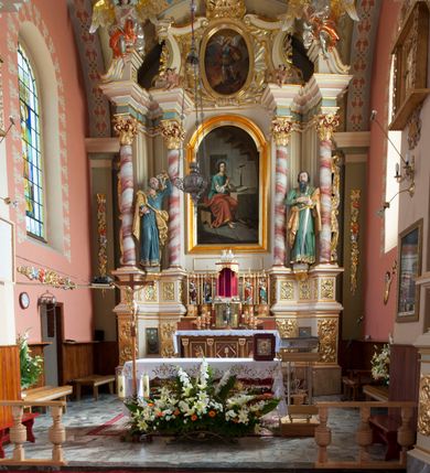 Zdjęcie nr 5: Nastawa ołtarzowa architektoniczna, jednoosiowa, jednokondygnacyjna ze zwieńczeniem, na podwójnym cokole. Ołtarz drewniany, prostopadłościenny; mensa drewniana z kamiennym portatylem. Antepedium podzielone na trzy pola czterema półkolumnami o stylizowanych kapitelach. W polach płyciny; w środkowej romb z płaskorzeźbionym kielichem z hostią; w zewnętrznych winne grona z kłosami zbóż.Tabernakulum w formie drewnianej skrzynki obitej blachą. Drzwiczki w kształcie stojącego prostokąta z aplikowaną, odlewaną plakietką ze sceną modlitwy Chrystusa w Ogrójcu, w narożach aplikowane uskrzydlone główki anielskie, całość w opasce dekorowanej różami. Tabernakulum w drewnianej obudowie, ściana frontowa flankowana parą kolumn. Tron wystawienia w formie niszy ujętej kolumienkami z łukiem o fantazyjnym wykroju. Całość zwieńczona rzeźbioną figurką Baranka Eucharystycznego leżącego na księdze. Po bokach tabernakulum stoją dwie pary nisz na postumentach z figurami czterech ewangelistów. Kondygnacja nastawy ujęta dwiema parami kolumn o kapitelach kompozytowych, stojących na tle zwielokrotnionych pilastrów. Podpory dźwigają fragmenty wyłamanego belkowania, zewnętrzna para również przerwany, wklęsło-wypukły przyczółek. Cokoły ustawione delikatnie pod kątem, zwrócone na zewnątrz. Na gzymsie wewnętrznych podpór niewielkie figurki puttów; na przyczółkach figury siedzących aniołów ubranych w długie suknie, okryte czerwonymi płaszczami. Między kolumnami na wspornikach figury św. Piotra i św. Pawła. W polu środkowym obraz św. Aleksego w profilowanej ramie w kształcie stojącego prostokąta zamkniętego łukiem półkolistym nadwieszonym. Zwieńczenie w formie leżącego prostokąta, ujętego masywnymi spływami wolutowymi, zamkniętego przeciwstawnie zwróconymi esownicami. W polu obraz św. Michała Archanioła w profilowanej ramie w formie stojącego owalu. Dolne partie cokołu dekorowane płaskorzeźbionym, stylizowanym akantem o układzie geometrycznym; wyższe z ornamentem w płycinach. Kondygnacja ujęta uszakami utworzonymi z karbowanej wstęgi przeplatającej się z ornamentem roślinnym. Woluty zwieńczenia dekorowane liśćmi palmowymi i kampanullami. Obraz w polu ujęty muszlami i liśćmi palmowymi; całość zwieńczona muszlą. Struktura polichromowana w odcieniu bieli; płyciny i fryz polichromowane na seledynowo, profile w odcieniu jasnego różu; trzony kolumn marmoryzowane; ornamentyka, kapitele, profile i ornamenty złocone i srebrzone.