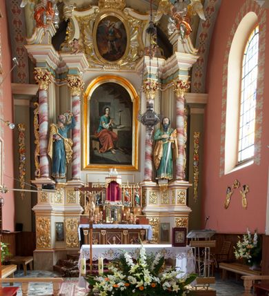 Zdjęcie nr 3: Nastawa ołtarzowa architektoniczna, jednoosiowa, jednokondygnacyjna ze zwieńczeniem, na podwójnym cokole. Ołtarz drewniany, prostopadłościenny; mensa drewniana z kamiennym portatylem. Antepedium podzielone na trzy pola czterema półkolumnami o stylizowanych kapitelach. W polach płyciny; w środkowej romb z płaskorzeźbionym kielichem z hostią; w zewnętrznych winne grona z kłosami zbóż.Tabernakulum w formie drewnianej skrzynki obitej blachą. Drzwiczki w kształcie stojącego prostokąta z aplikowaną, odlewaną plakietką ze sceną modlitwy Chrystusa w Ogrójcu, w narożach aplikowane uskrzydlone główki anielskie, całość w opasce dekorowanej różami. Tabernakulum w drewnianej obudowie, ściana frontowa flankowana parą kolumn. Tron wystawienia w formie niszy ujętej kolumienkami z łukiem o fantazyjnym wykroju. Całość zwieńczona rzeźbioną figurką Baranka Eucharystycznego leżącego na księdze. Po bokach tabernakulum stoją dwie pary nisz na postumentach z figurami czterech ewangelistów. Kondygnacja nastawy ujęta dwiema parami kolumn o kapitelach kompozytowych, stojących na tle zwielokrotnionych pilastrów. Podpory dźwigają fragmenty wyłamanego belkowania, zewnętrzna para również przerwany, wklęsło-wypukły przyczółek. Cokoły ustawione delikatnie pod kątem, zwrócone na zewnątrz. Na gzymsie wewnętrznych podpór niewielkie figurki puttów; na przyczółkach figury siedzących aniołów ubranych w długie suknie, okryte czerwonymi płaszczami. Między kolumnami na wspornikach figury św. Piotra i św. Pawła. W polu środkowym obraz św. Aleksego w profilowanej ramie w kształcie stojącego prostokąta zamkniętego łukiem półkolistym nadwieszonym. Zwieńczenie w formie leżącego prostokąta, ujętego masywnymi spływami wolutowymi, zamkniętego przeciwstawnie zwróconymi esownicami. W polu obraz św. Michała Archanioła w profilowanej ramie w formie stojącego owalu. Dolne partie cokołu dekorowane płaskorzeźbionym, stylizowanym akantem o układzie geometrycznym; wyższe z ornamentem w płycinach. Kondygnacja ujęta uszakami utworzonymi z karbowanej wstęgi przeplatającej się z ornamentem roślinnym. Woluty zwieńczenia dekorowane liśćmi palmowymi i kampanullami. Obraz w polu ujęty muszlami i liśćmi palmowymi; całość zwieńczona muszlą. Struktura polichromowana w odcieniu bieli; płyciny i fryz polichromowane na seledynowo, profile w odcieniu jasnego różu; trzony kolumn marmoryzowane; ornamentyka, kapitele, profile i ornamenty złocone i srebrzone.