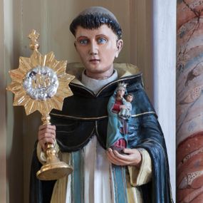 Zdjęcie nr 1: Rzeźba drążona z tyłu przedstawiająca stojącą na niewysokim, prostopadłościennym cokole postać św. Jacka Odrowąża. Święty jest ustawiony frontalnie, w lekkim kontrapoście, z prawym kolanem zgiętym. Twarz ma owalną, o delikatnych, młodzieńczych rysach, z jasnymi oczami, wąskim nosem i niewielkimi ustami; na głowie wycięta tonsura. Jest ubrany w strój dominikański: biały habit ze szkaplerzem i czarny płaszcz z kapturem, pod nim ma błękitną stułę. W lewej dłoni trzyma figurkę Madonny z Dzieciątkiem, w prawej monstrancję. Polichromia w partiach ciała naturalistyczna.