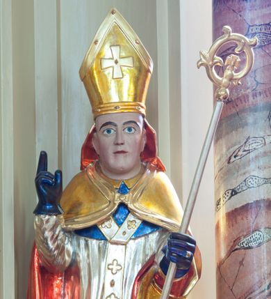 Zdjęcie nr 1: Figura drążona, na cokole. Święty Stanisław przedstawiony w całej postaci, stojący frontalnie, obie ręce ma zgięte w łokciach, prawą unosi do góry, lewą przytrzymuje pastorał. Stanisław ma pociągła twarz z dużymi, szeroko otwartymi oczami, szerokim nosem i wąskimi ustami. Jest ubrany w strój biskupi: niebieską albę, białą rokietę zdobioną złotym pasem koronki przy dolnej krawędzi i paliusz z aplikowanymi krzyżami greckimi. Na to założoną ma obszerną, złotą kapę podbitą czerwienią, która spięta pod szyją okrywa ramiona i spływa do ziemi; na głowie ma infułę, a na rękach niebieskie rękawiczki. Polichromia w odkrytych partiach karnacji postaci jest traktowana naturalistycznie.