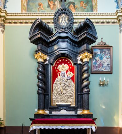 Zdjęcie nr 1: Ołtarz prostopadłościenny, w typie tumbowym, z mensą o brzegu zdobionym rzędem liści akantu naprzemian z łukami kotarowymi zwieńczonymi kulami oraz podwieszonym lambrekinem. Nastawa ołtarzowa jest architektoniczna, jednoosiowa ze zwieńczeniem, ujęta przez kolumny stojące na ukośnie dostawionych cokołach. Kolumny w jednej trzeciej kanelowane w dwóch trzecich skręcone z wplecioną wicią roślinną, ze złoconym kapitelem podtrzymują przerwany przyczółek ze ślimacznicami. Belkowanie bogato profilowane nad częścią środkową jest wyłamane trzema wklęsłymi łukami. W szczycie owalny medalion z monogramem ”MARIA”, w obramieniu z wieńca laurowego, ślimacznic i festonów, zakończony krzyżem. W osi środkowej prostokątna wnęka w profilowanym obramieniu, zamknięta półkolistym łukiem nadwieszonym z obrazem Matki Boskiej z Dzieciątkiem. 