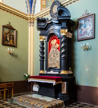 Zdjęcie nr 6: Ołtarz prostopadłościenny, w typie tumbowym, z mensą o brzegu zdobionym rzędem liści akantu naprzemian z łukami kotarowymi zwieńczonymi kulami oraz podwieszonym lambrekinem. Nastawa ołtarzowa jest architektoniczna, jednoosiowa ze zwieńczeniem, ujęta przez kolumny stojące na ukośnie dostawionych cokołach. Kolumny w jednej trzeciej kanelowane w dwóch trzecich skręcone z wplecioną wicią roślinną, ze złoconym kapitelem podtrzymują przerwany przyczółek ze ślimacznicami. Belkowanie bogato profilowane nad częścią środkową jest wyłamane trzema wklęsłymi łukami. W szczycie owalny medalion z monogramem ”MARIA”, w obramieniu z wieńca laurowego, ślimacznic i festonów, zakończony krzyżem. W osi środkowej prostokątna wnęka w profilowanym obramieniu, zamknięta półkolistym łukiem nadwieszonym z obrazem Matki Boskiej z Dzieciątkiem. 