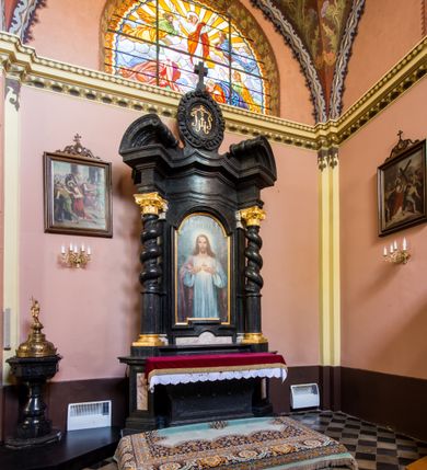 Zdjęcie nr 6: Ołtarz prostopadłościenny, w typie tumbowym, z mensą o brzegu zdobionym rzędem liści akantu naprzemian z łukami kotarowymi zwieńczonymi kulami oraz podwieszonym lambrekinem. Nastawa ołtarzowa jest architektoniczna, jednoosiowa ze zwieńczeniem, ujęta przez kolumny stojące na ukośnie dostawionych cokołach. Kolumny w jednej trzeciej kanelowane w dwóch trzecich skręcone z wplecioną wicią roślinną, ze złoconym kapitelem podtrzymują przerwany przyczółek ze ślimacznicami. Belkowanie bogato profilowane nad częścią środkową jest wyłamane trzema wklęsłymi łukami. W szczycie owalny medalion z monogramem "IHS”, w obramieniu z wieńca laurowego, ślimacznim z festonami, zakończony krzyżem. W osi środkowej prostokątna wnęka w profilowanym obramieniu, zamknięta półkolistym łukiem nadwieszonym z obrazem Najświętszego Serca Jezusowego. 


