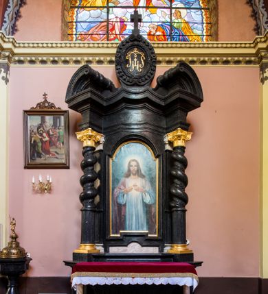 Zdjęcie nr 1: Ołtarz prostopadłościenny, w typie tumbowym, z mensą o brzegu zdobionym rzędem liści akantu naprzemian z łukami kotarowymi zwieńczonymi kulami oraz podwieszonym lambrekinem. Nastawa ołtarzowa jest architektoniczna, jednoosiowa ze zwieńczeniem, ujęta przez kolumny stojące na ukośnie dostawionych cokołach. Kolumny w jednej trzeciej kanelowane w dwóch trzecich skręcone z wplecioną wicią roślinną, ze złoconym kapitelem podtrzymują przerwany przyczółek ze ślimacznicami. Belkowanie bogato profilowane nad częścią środkową jest wyłamane trzema wklęsłymi łukami. W szczycie owalny medalion z monogramem &quot;IHS”, w obramieniu z wieńca laurowego, ślimacznim z festonami, zakończony krzyżem. W osi środkowej prostokątna wnęka w profilowanym obramieniu, zamknięta półkolistym łukiem nadwieszonym z obrazem Najświętszego Serca Jezusowego. 


